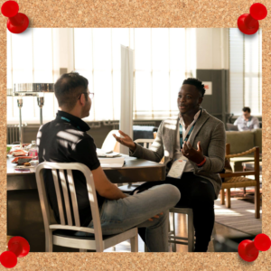 Image depicts two working men chatting over a table.