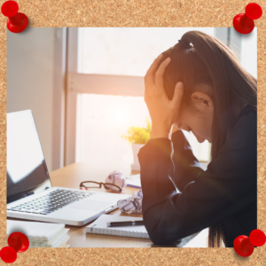 Business woman slouches over her desk with her head in her hands.