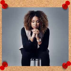 Female worker is shown with clasped hands as she sits in an office chair, hunched over. She appears to be in prayer.