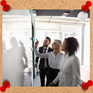 Employee development opportunities can be in a classroom setting, like this photo. One businesswoman writes on a whiteboard while two other employees look on.