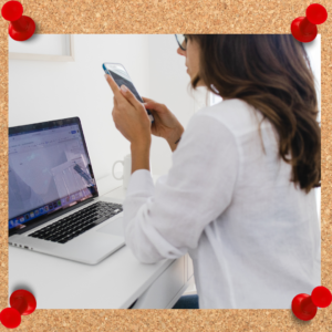 Image depicts female employee scrolling her phone while seated in front of a computer.