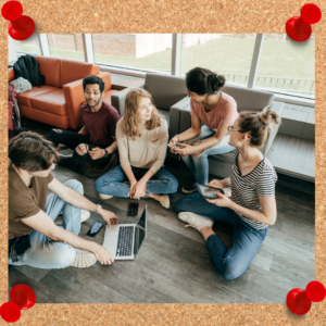 Image depicts a group of colleagues sitting on the floor and in chairs as they communicate around a laptop.